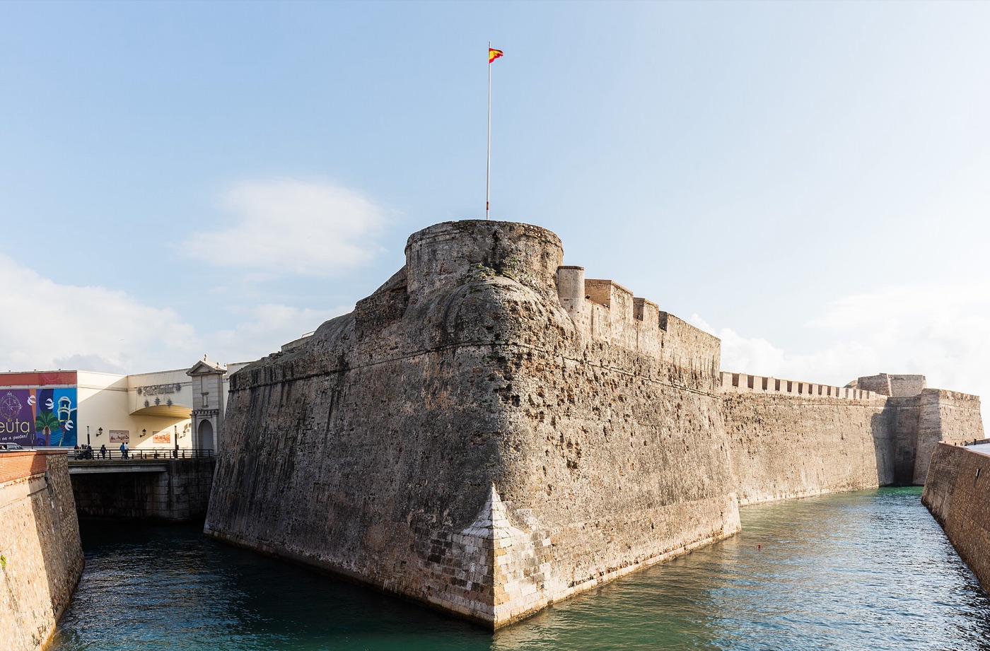 Las Murallas Reales de Ceuta, con la bandera de España en lo alto del baluarte y el foso de agua a sus pies