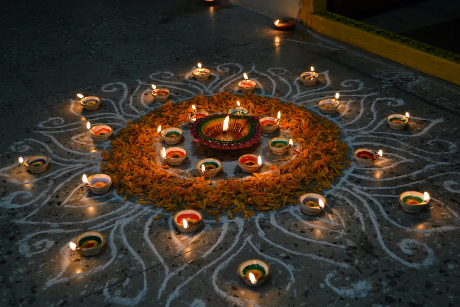 Círculo de lámparas de barro encendidas sobre un rangoli de líneas blancas y pétalos de caléndula, con una diya grande en el centro, en la noche del Diwali