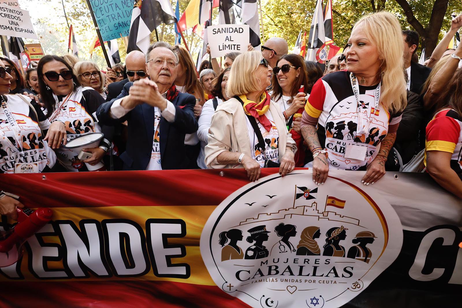 Multitud con camisetas y pancartas tras una gran pancarta de Mujeres Caballas con la bandera de España.