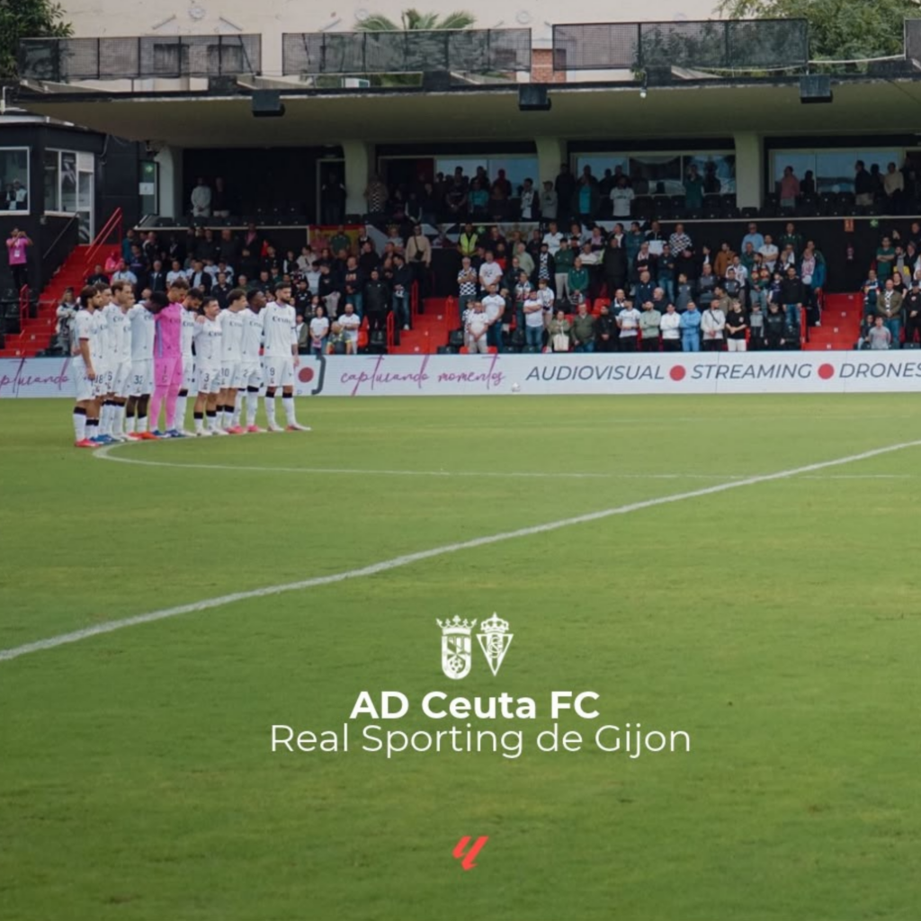 Jugadores de fútbol con equipación blanca alineados en el césped ante una grada con público.