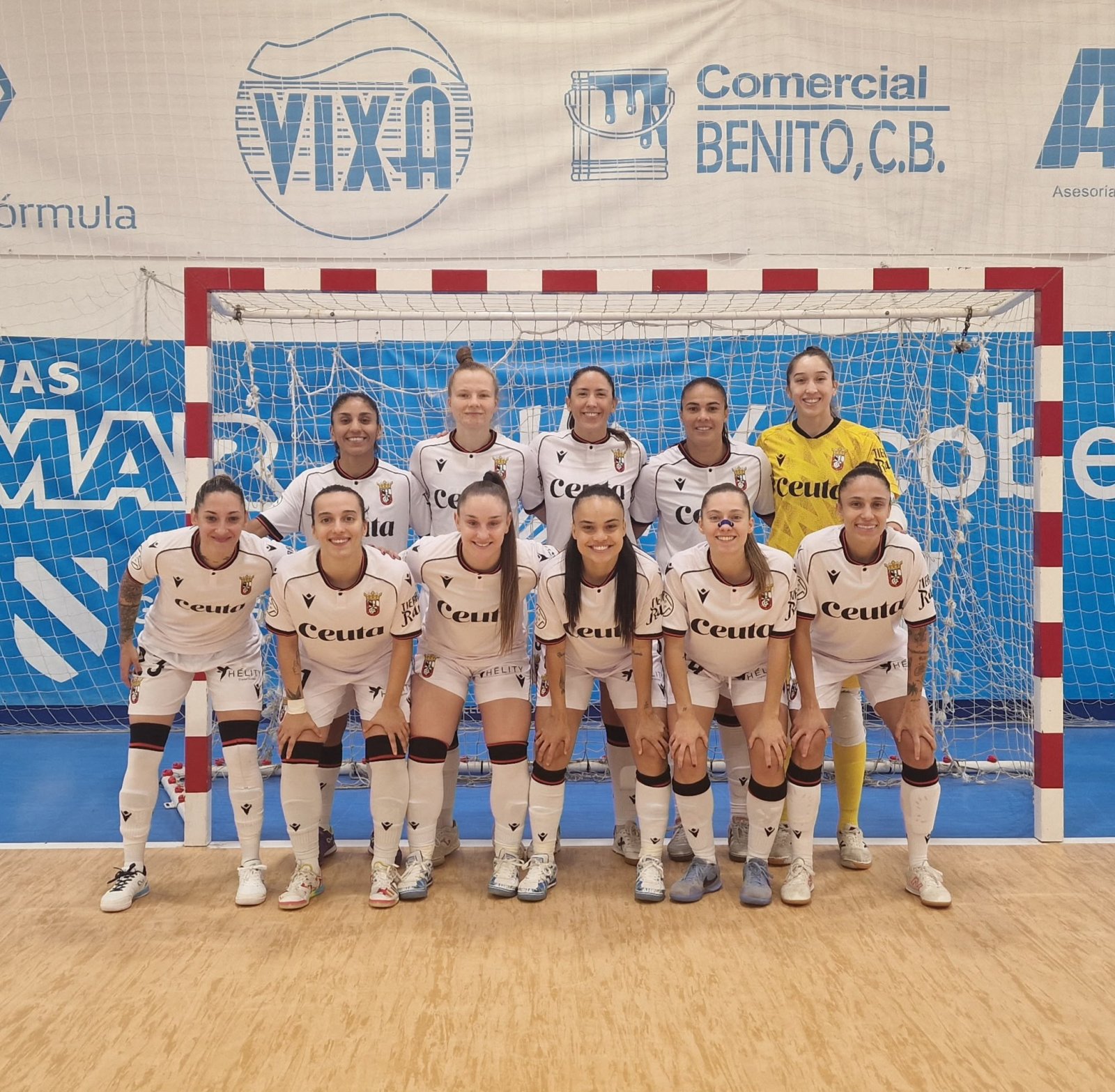 Un equipo femenino de fútbol sala, con camisetas blancas y una portera de amarillo, posa en fila delante de una portería.