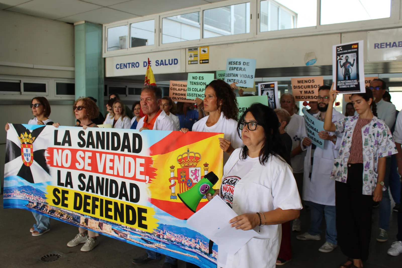 Personas con batas blancas sostienen una pancarta reivindicativa sobre sanidad ante la entrada de un centro de salud.