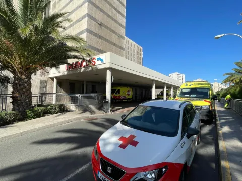 Ambulancias y un coche con cruz roja junto a la entrada de Urgencias de un hospital, bajo una marquesina.